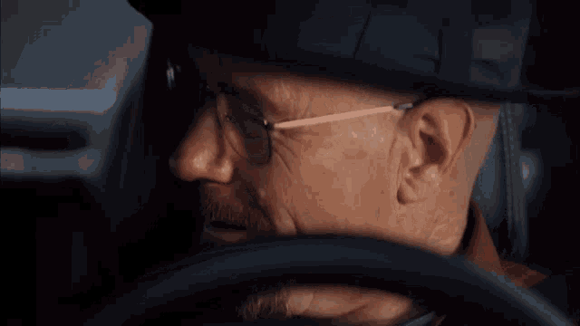 a man in a hat and glasses is driving a car