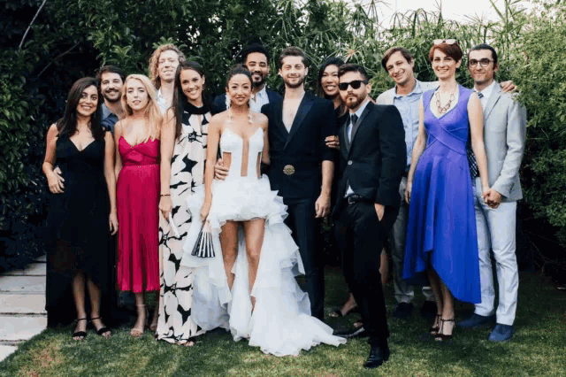 a group of people posing for a picture including a bride in a short white dress