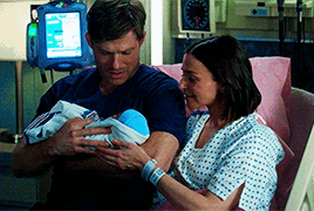 a man and a woman are holding a baby in a hospital bed .