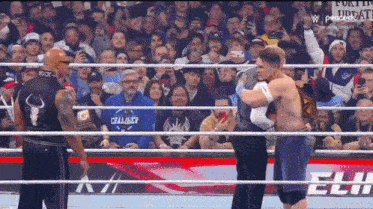 a wrestler is hugging another wrestler in a ring while a crowd watches .