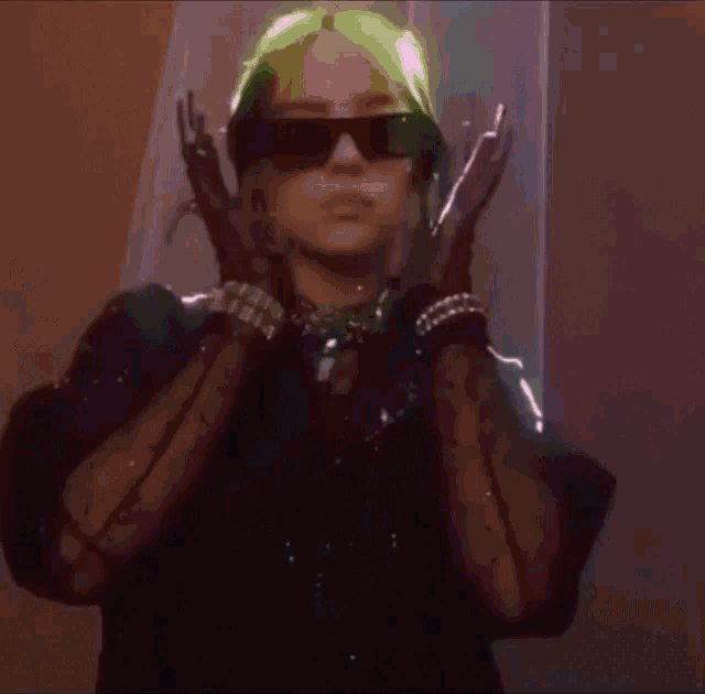 billie eilish is wearing sunglasses and gloves while standing in a room .