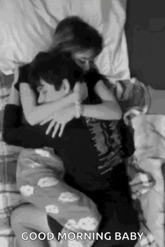 a black and white photo of a man and a woman hugging each other on a bed .