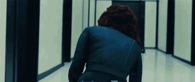 a woman with red hair is walking down a hallway in a blue jacket .