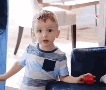 a little boy is sitting on a blue couch playing with a toy .