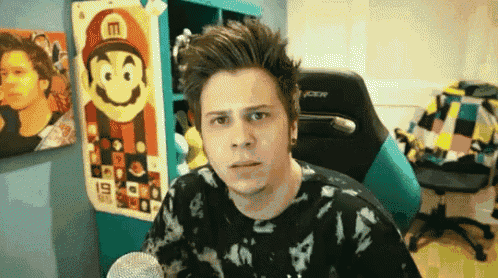 a man is sitting in front of a microphone in a room with a mario poster on the wall behind him