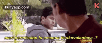 two men are standing next to each other and talking to each other in a park .