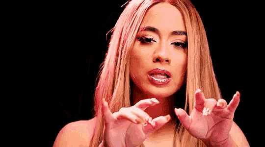 a woman with long blonde hair and pink lipstick is making a funny face with her hands outstretched .