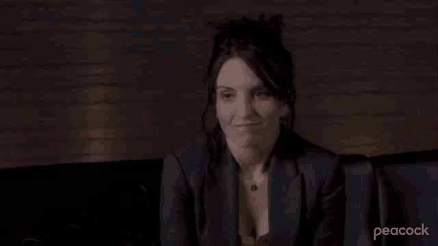 a woman in a suit is sitting on a couch with the word sure in front of her .