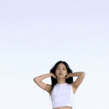 a woman in a white crop top and blue jeans is standing in front of a white background .