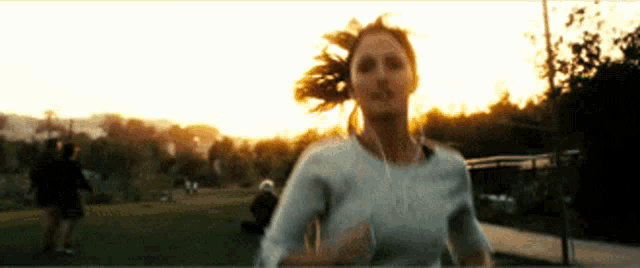 a woman wearing headphones is running through a park at sunset