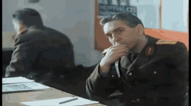 a man in a military uniform sitting at a desk with his hand on his chin