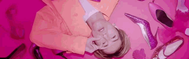 a woman in a pink suit is laying on a pink floor surrounded by pink shoes .