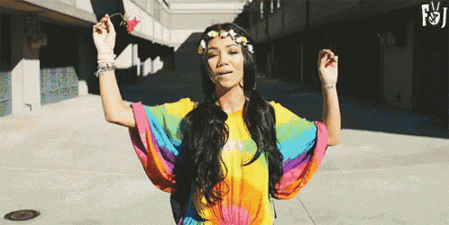 a woman wearing a rainbow tie dye shirt and a flower crown is dancing .