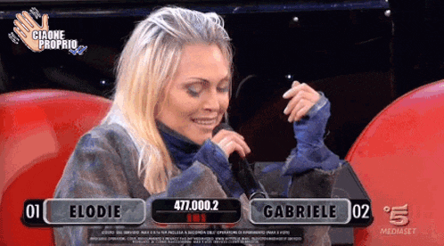a woman is singing into a microphone while sitting in front of a sign that says gabriele