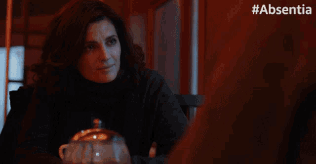 a woman sits at a table with a cup of coffee in front of a #absentia sign