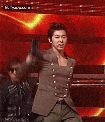 a man in a suit is dancing on a stage while another man looks on .