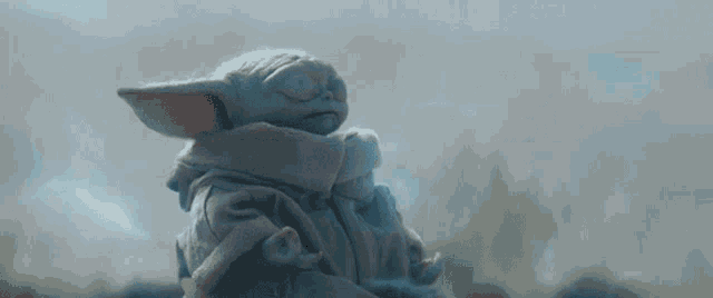 a baby yoda figurine is sitting in a lotus position with its eyes closed .