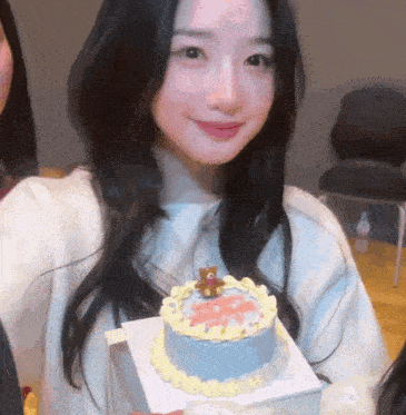 a girl is holding a small cake with a teddy bear on it and smiling .