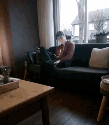 a man is sitting on a couch in front of a window looking at his phone