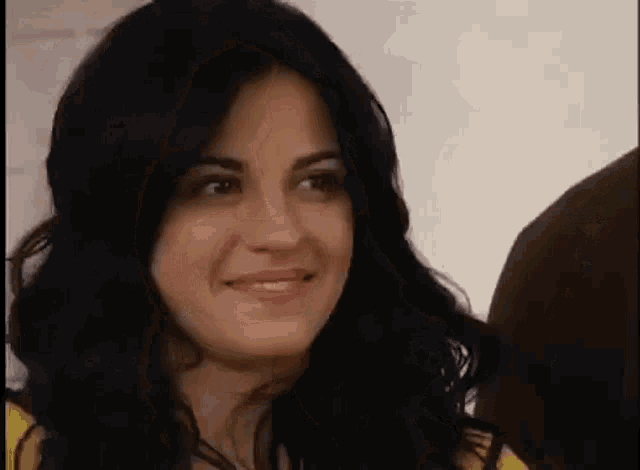 a woman with long black hair is smiling and looking at the camera while standing next to a man .