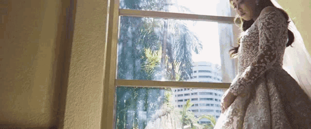 a bride in a wedding dress is standing in front of a window