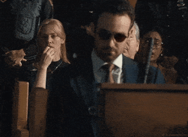 a man in a suit and tie stands in front of a podium while a woman covers her mouth .
