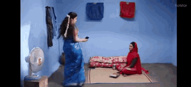 two women are standing next to each other in a room with a fan .