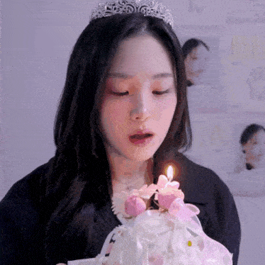 a woman with a tiara on her head blows out a candle on a cake