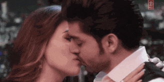 a man and a woman are kissing in front of a sign that says t