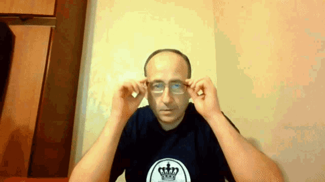 a man wearing glasses and a shirt with a crown on it adjusts his glasses