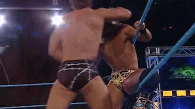 two men are wrestling in a wrestling ring and one of them is wearing shorts .