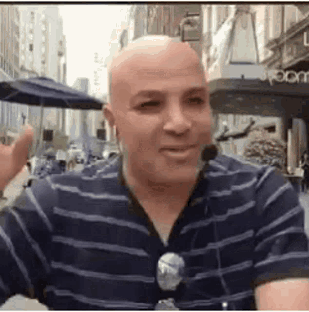 a bald man wearing a striped shirt and sunglasses is sitting at a table in front of a microphone .