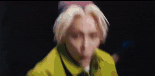 a man with blue hair is wearing a yellow turtleneck sweater and blue gloves .