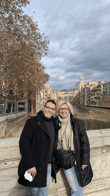 a man and a woman are posing for a picture on a bridge over a river