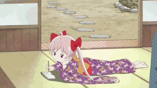 a girl in a kimono is laying on the floor writing