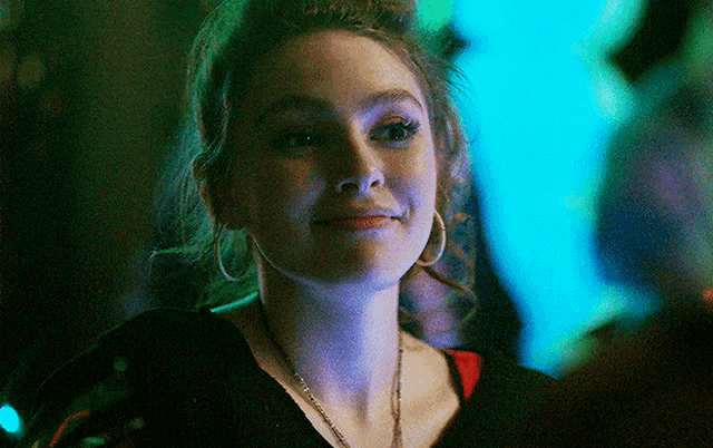 a woman wearing hoop earrings and a necklace smiles for the camera