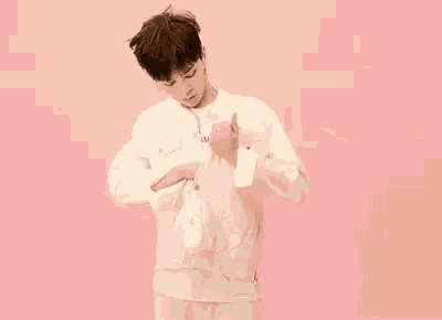 a young man wearing a white shirt and earrings is standing in front of a pink wall .