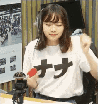 a woman wearing headphones and a white t-shirt with chinese characters on it is holding a microphone .
