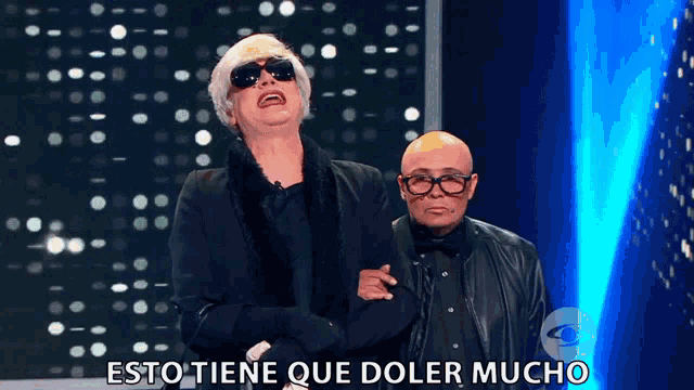 a man in sunglasses stands next to another man with the words " esto tiene que doler mucho " below him