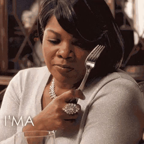 a woman is holding a fork to her mouth while sitting at a table with a glass of wine .