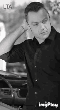 a man in a black shirt is standing in front of a car and holding his head .