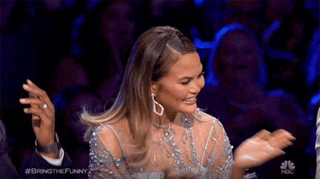 a woman in a feathered dress is applauding in front of a nbc sign