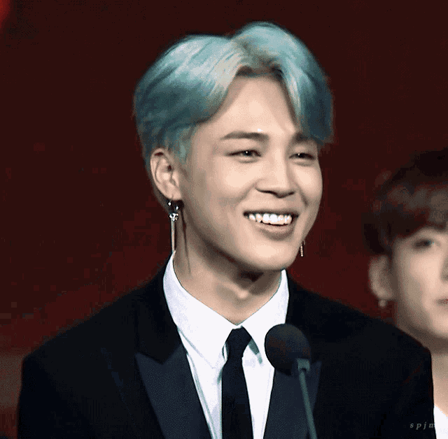 a man with blue hair is smiling while wearing a suit