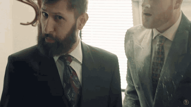 a man with a beard is standing next to another man wearing a suit and tie