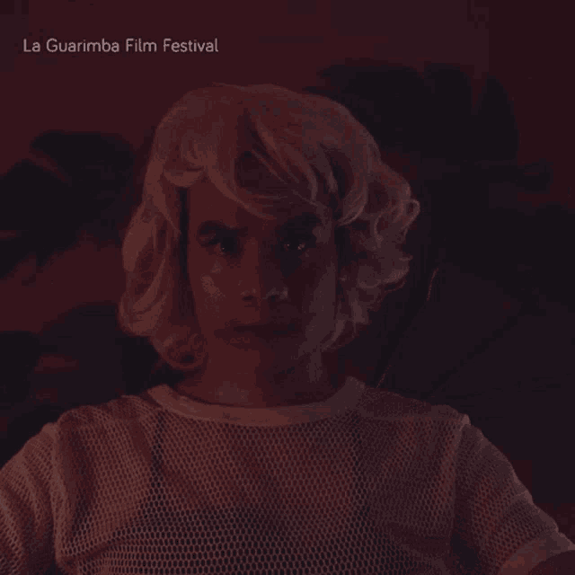 a woman wearing a wig and a white shirt with la guarimba film festival written on the top
