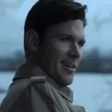 a man in a trench coat is smiling and looking to the side .