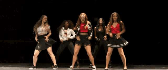 a group of women are dancing on a stage with one wearing a shirt that says i love
