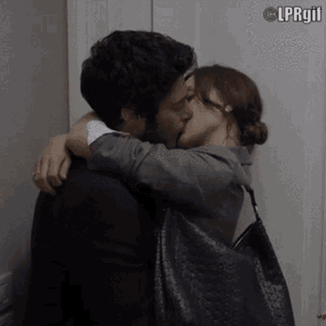 a man and a woman are kissing in front of a white wall . the woman is holding a purse .