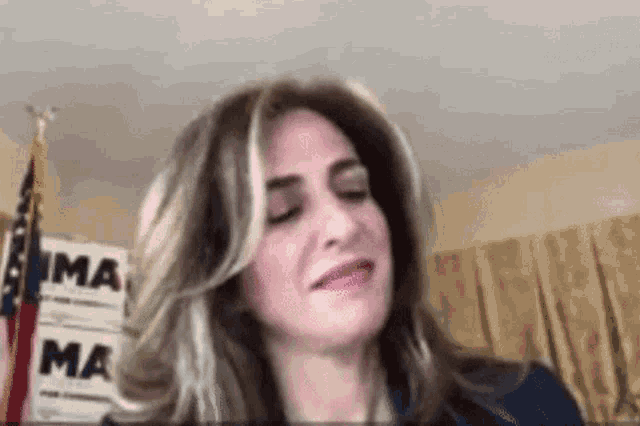 a woman is making a funny face with her eyes closed in front of a flag .