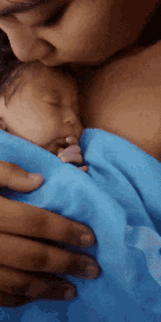 a woman is holding a baby wrapped in a blue blanket and kissing it on the forehead